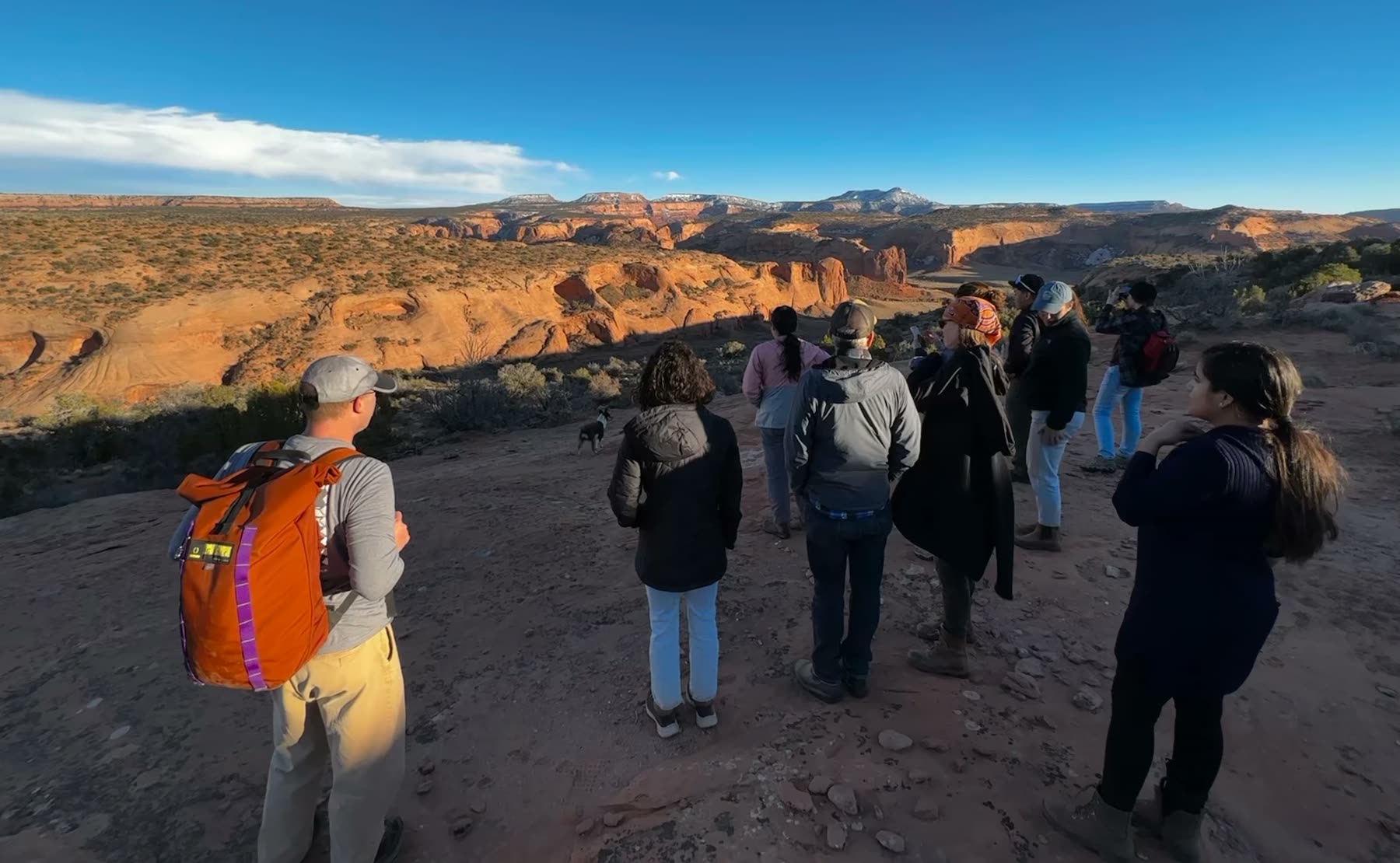 A small group standing on a canyon rim in winter light, looking out over red rock and snow-topped mesas.