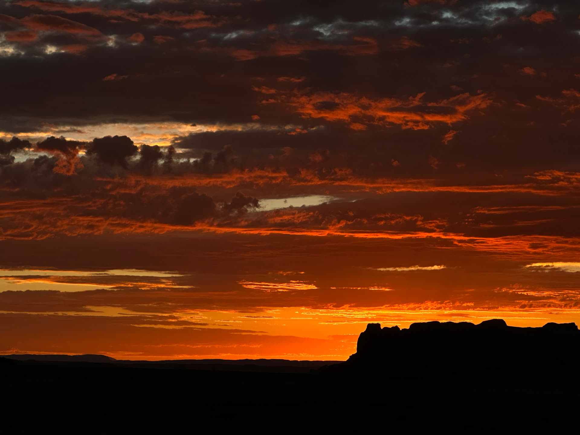Deep orange and red sunset burning behind the silhouette of a flat-topped mesa on the Navajo Nation.