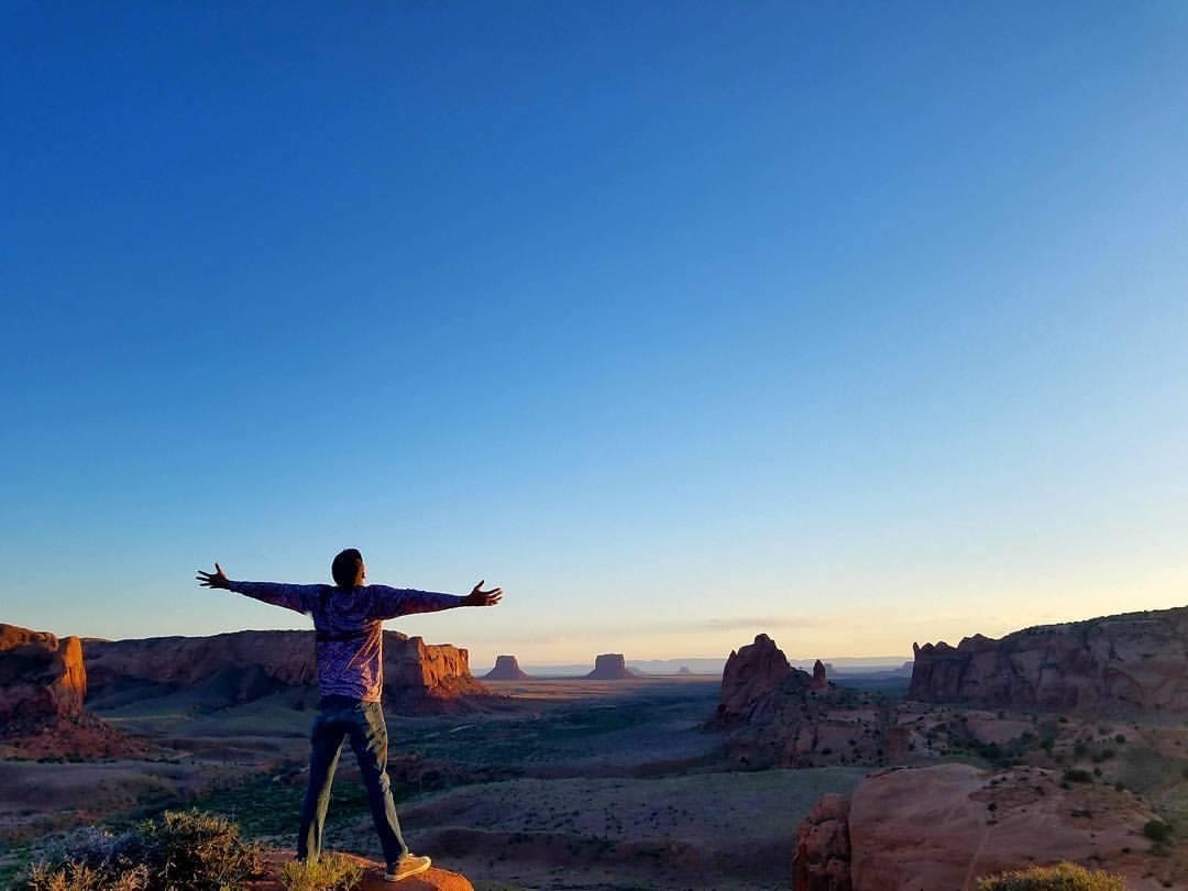 Tim Benally standing with his arms outstretched above the canyon landscape at sunset.